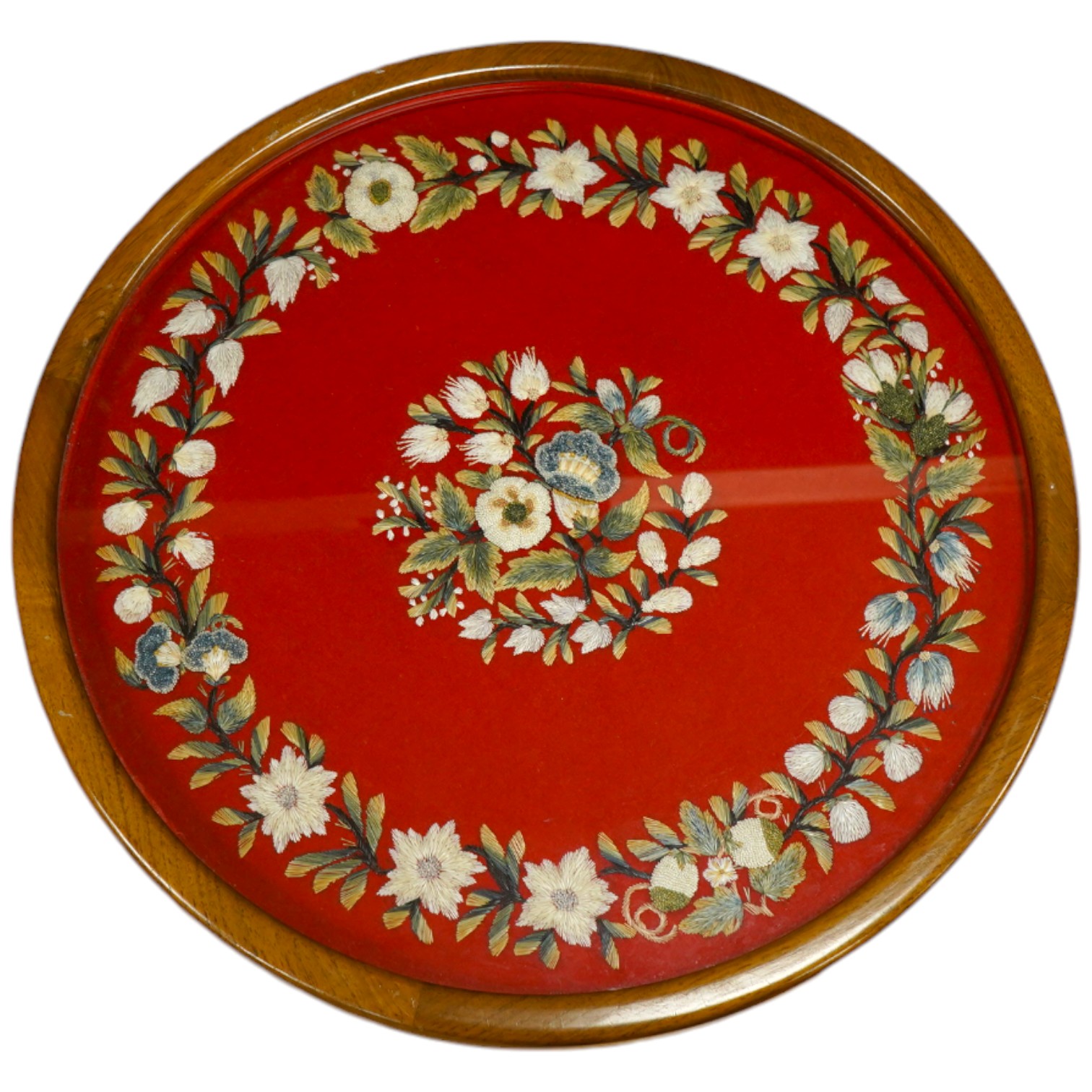 A framed, 19th century, possibly Scandinavian, red felt circular multi-coloured silk embroidery of flowers, acorns and leaves, also embroidered with fine stump work style beadwork flower detail, 32cm diameter. Condition